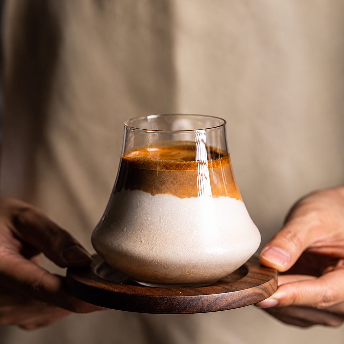 ガラスカップのカフェラテを木製トレーに載せて手で持つ使用シーン